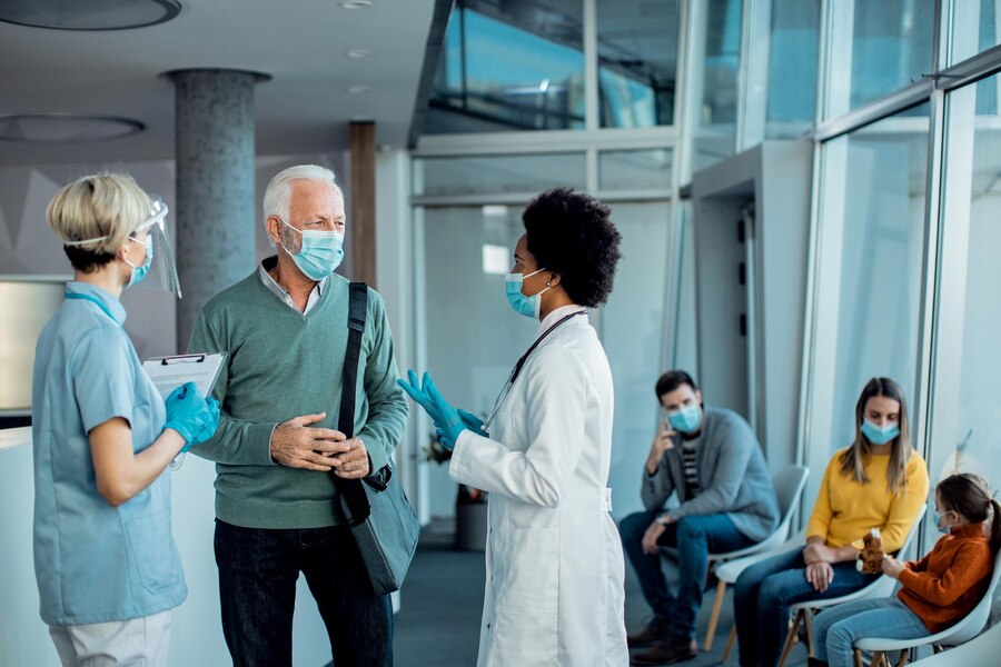 senior-man-with-protective-face-mask-talking-doctors-hospital-hallway_